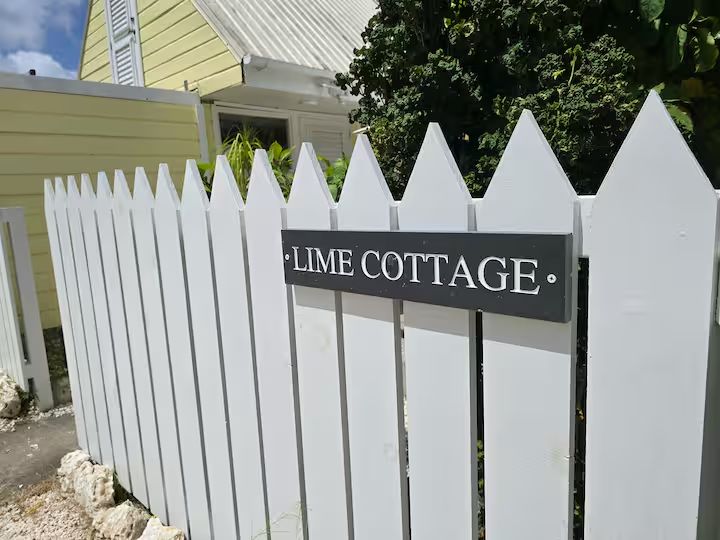 Lime Cottage welcome sign — dark grey wooden plaque on the white picket fence
